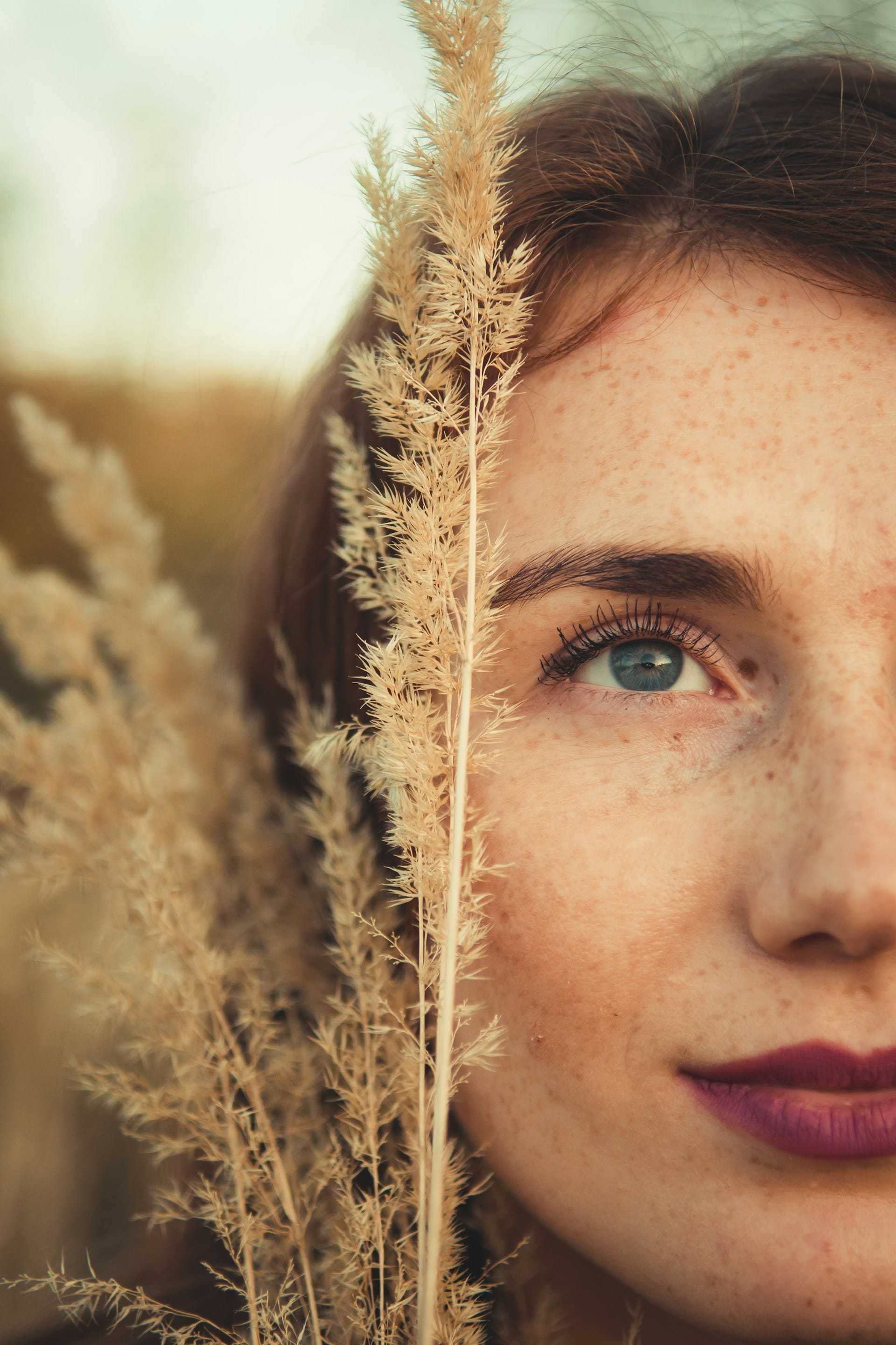 Close-up of a woman's face partially obscured by tall dry grass.